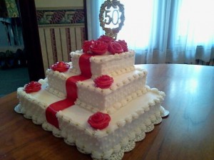 A very special cake for a very special occasion.  This 3 tier Sour Cream Almond Cake is filled and frosted with homemade buttercream frosting and finished with individually handcrafted buttercream roses, gold dragees and red satin ribbon.  Stunning! 